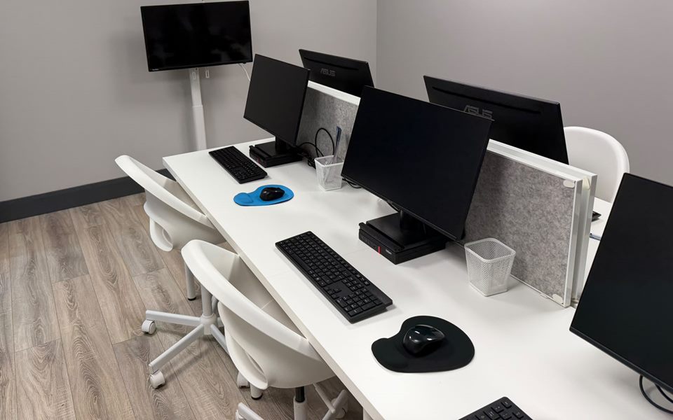 Shared desks with monitors, keyboards and white chairs in the Pefwil workspace